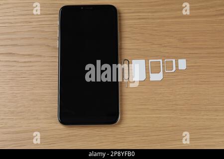 SIM cards, mobile phone and ejector tool on wooden table, flat lay Stock Photo