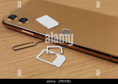 SIM cards, mobile phone and ejector tool on wooden table Stock Photo