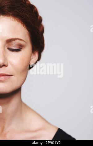 Not a hair out of place. Studio shot of a beautiful redhead woman with a braided up-do posing against a gray background. Stock Photo