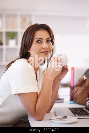 Daydreaming during her coffee break. A young woman enjoying a coffee break at her desk. Stock Photo