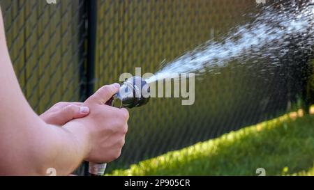 Hose watering plants in the garden by the farmer. Watering with gun nozzle. Shallow depth of field. Stock Photo