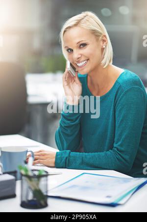 Tackling her work with a can-do attitude. a businesswoman talking on her cellphone while sitting at her office desk. Stock Photo