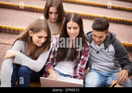 Working on their latest assignment. High angle of a group of university students using a laptop on campus. Stock Photo