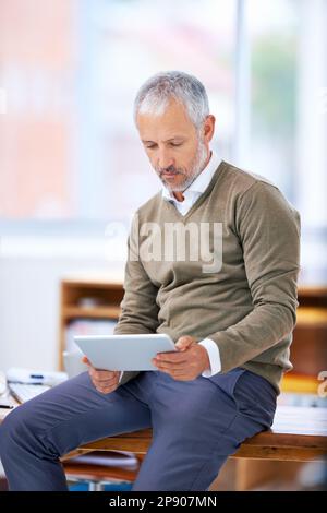 Analyzing facts and figures. A mature businessman sitting on his desk working on a tablet. Stock Photo
