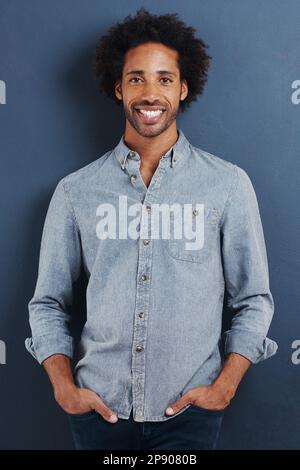 A mans gotta be confident. Portrait of a handsome young man standing with his hands in his pockets on a gray background. Stock Photo
