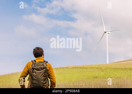 Man looking on the wind power mill among green hills Stock Photo
