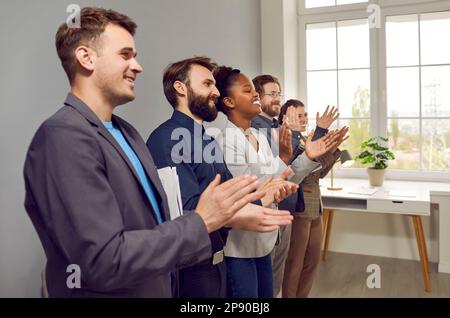 Multinational people working in same company applaud stand in office along wall Stock Photo