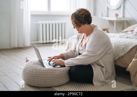 Smiling middle aged plus size woman working on laptop from home Stock Photo