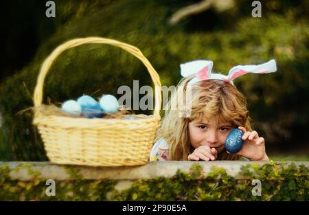 Child with rabbit ears, Easter holidays. Kid hunting Easter eggs in easters basket. Cute bunny boy, funny kids portrait. Stock Photo