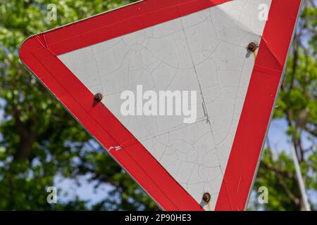 Close-up of give way road sign. Red and white triangle. Green trees and blue sky on background. Stock Photo