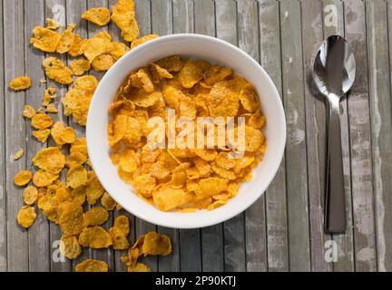 Top view of appetizing corn flakes in white bowl with milk placed on striped wooden table near spoon Stock Photo