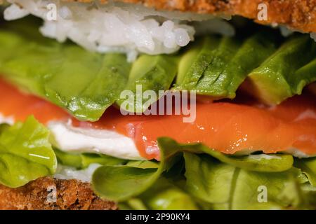 Closeup of a freshly prepared raw salmon sandwich with avocado, cream cheese, fried rice and lettuce Stock Photo