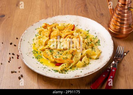 Pappardelle pasta with chicken fillet, garlic and chili sprinkled with parmesan cheese and chopped parsley, close up. The dish is served with cutlery Stock Photo