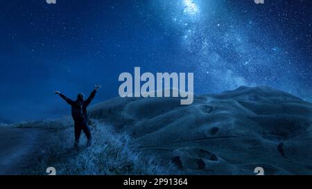 Person with raised arms under a starry night sky in the mountains Stock Photo