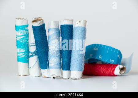 Blue threads and red in different shades on a spool and centimeter tape on a white isolated background, fashion and trend Stock Photo