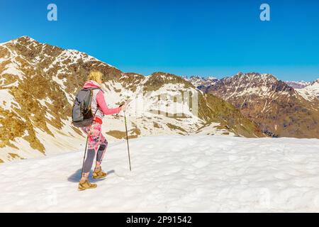 backside of backpacker woman climbing with trekking poles on top of Diavolezza col in Switzerland in Graubunden canton. Stock Photo