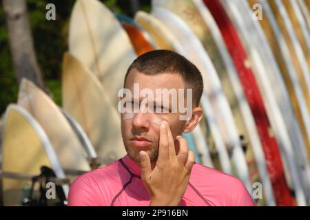 Man surfer applies protective zinc on his face. Preparing to surf. Best protection from active sun and UV while surfing. Eco-friendly product that is Stock Photo