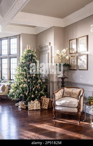 Christmas gifts under tree with armchair in Arts and Crafts style country house, Kent, UK Stock Photo