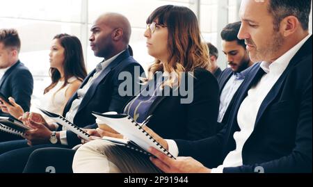 Interesting content is crucial to keeping an audience engaged. Shot of a group of businesspeople taking down notes while attending a conference. Stock Photo