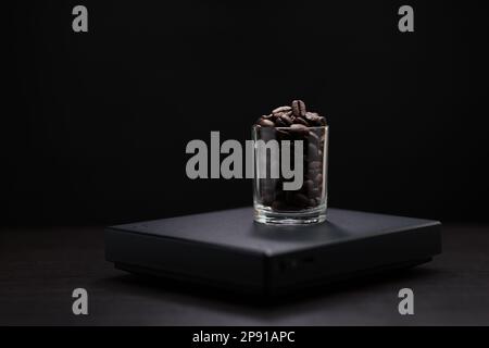 Dark roasted coffee beans in a clear glass on a black digital scale. Stock Photo