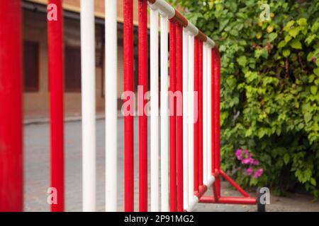 Metal red and white safety barrier on a road. Stop sign railing against green bushes Stock Photo