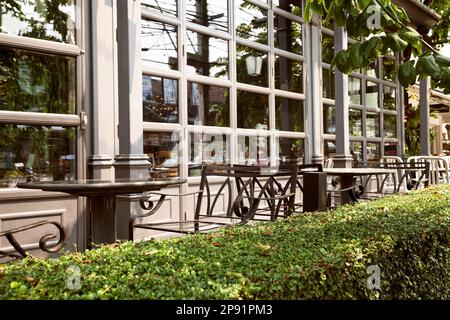 Empty outdoor cafe - metal forged furniture fenced by green hedge. Tables and chairs at restaurant terrace Stock Photo