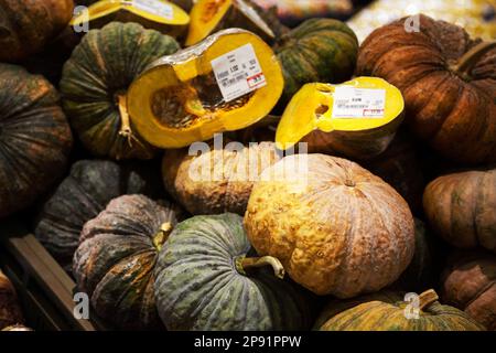 Pile of pumpkins with price tags at a supermarket. Many green and brown vegetables whole and cut in halves background Stock Photo