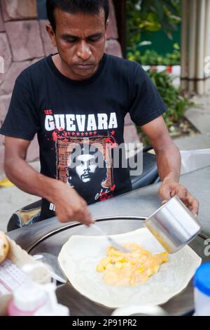 Pattaya, Thailand - March 22, 2016: Indian man cooking a crepe stuffed with mango on a street food cart in Thailand, wearing Che Guevara T-shirt Stock Photo