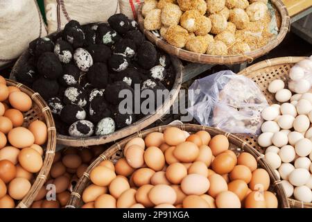 Several baskets of raw and cooked eggs at Vietnamese market. Pile of Asian delicacy black century eggs in ash Stock Photo