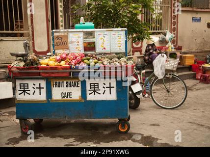 Street vendor cart selling tropical fruit and making drinks. Outdoor stand with fresh juice and other beverages. Text on the stall in Chinese: Fruit j Stock Photo