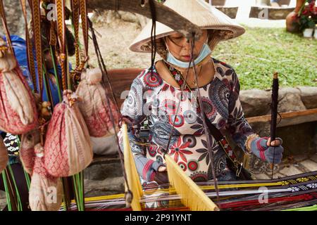 Nha Trang, Vietnam - March 31, 2018: Vietnamese lady weaver working on a loom, making handmade pattern textile. National weaving craft Stock Photo