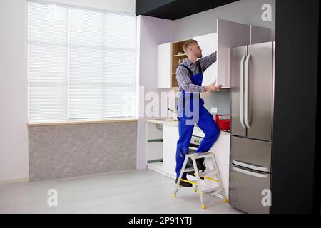 Male Carpenter Assembling White Cabinet On Wall In Kitchen Stock Photo