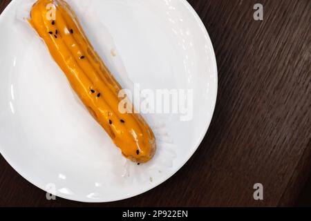 Eclair lays on the white saucer, it is a pastry made with choux dough filled with a cream and topped with a flavored icing. Top view Stock Photo