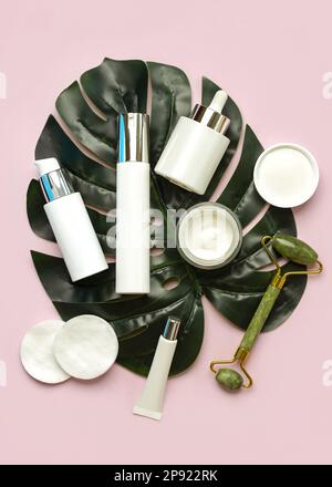 Set of cosmetics and jade massanger roller for skin care and beauty with green nature leaf over pink background. Skin care products concept Stock Photo