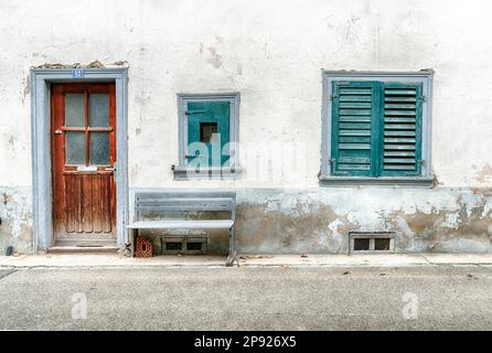Worn and faded house front detail with two windows and old wooden door and rickety bench on the roadside in the idyllic village of Neunkirch in Stock Photo