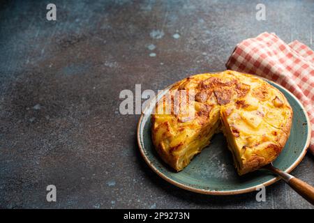 Homemade Spanish tortilla with one slice cut - omelette with potatoes on plate on stone rustic background top view. Traditional dish of Spain Stock Photo