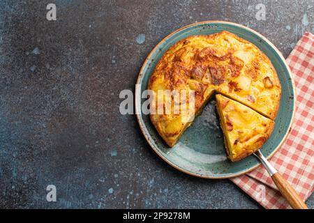 Homemade Spanish tortilla with one slice cut - omelette with potatoes on plate on stone rustic background top view. Traditional dish of Spain Stock Photo