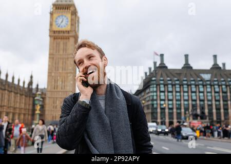 Happy bearded man talking on the phone while standing on the background of the Big Ben tower Stock Photo