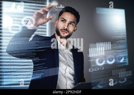 All the information is at my fingertips. Shot of a handsome young businessman standing alone in the office at night and using an interactive screen. Stock Photo