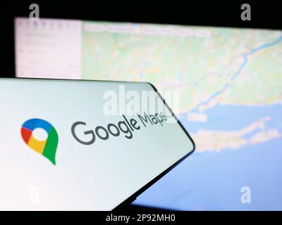 Smartphone with logo of web mapping platform Google Maps on screen in front of website. Focus on center-right of phone display. Stock Photo