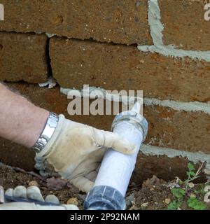 Image of the hands of a mason while filling joints in a tuff brick wall. Finishing work of DIY and construction. Stock Photo