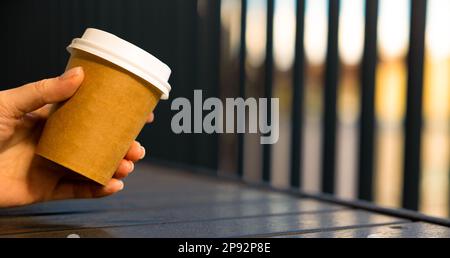 woman's hand holds paper cup with coffee with white lid Cafe open veranda Stock Photo