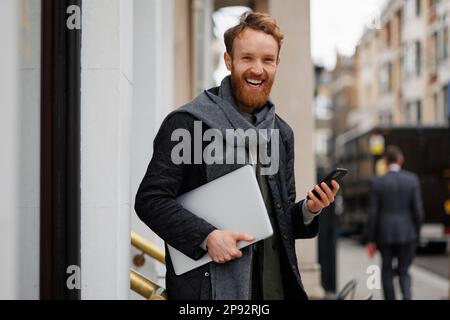 Happy business man with a laptop and smartphone in his hands is standing on the street of a big city Stock Photo