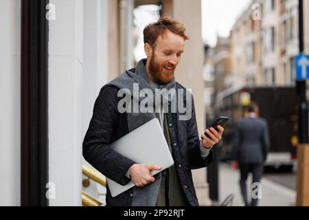 Happy business man with a laptop and smartphone in his hands is standing on the street of a big city Stock Photo
