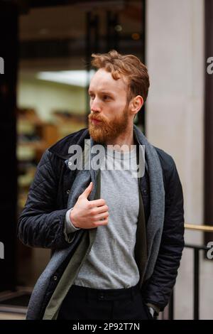 Bearded man in a jacket and scarf walks down the street Stock Photo