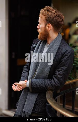 Portrait of a bearded brutal man leaning against the railing on the street Stock Photo