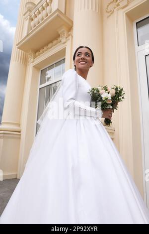 Young bride wearing wedding dress with beautiful bouquet outdoors Stock Photo