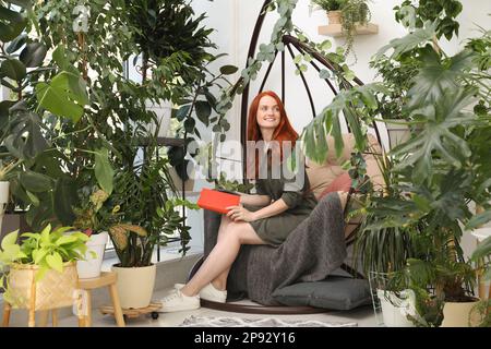 Happy beautiful woman with book in egg chair at home Stock Photo