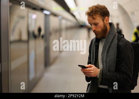 Man using smartphone on the platform of the subway station while waiting for the train Stock Photo