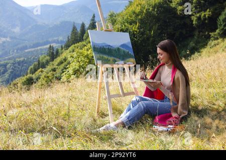 Young woman drawing on easel in mountains Stock Photo